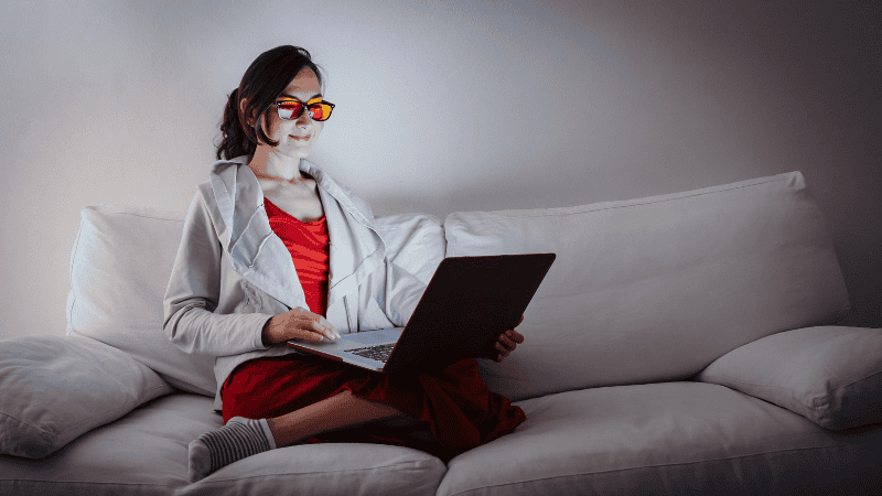 A person wearing amber-tinted blue light blocking glasses while reading a physical book under warm light to protect the circadian rhythm before bed.