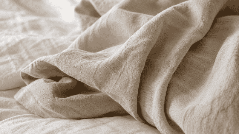 Close-up of soft breathable linen bedding in natural cream tones, representing lightweight sleep-friendly bedding for temperature regulation