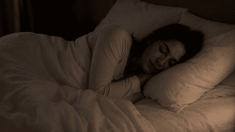 A person sleeping deeply in a dark, cool bedroom with white linen bedding, representing restful deep sleep at night
