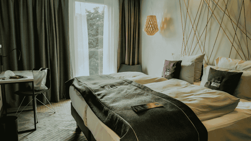 A dark, serene bedroom "cave" optimized for deep sleep featuring blackout curtains, clean bedding, and a cool color palette to support melatonin production.