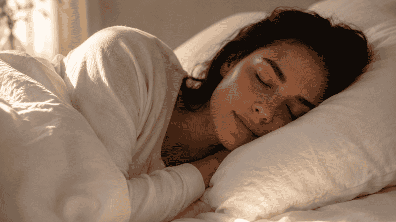 A person sleeping peacefully in soft morning light with white linen bedding, representing finally returning to restful sleep after a 3am waking