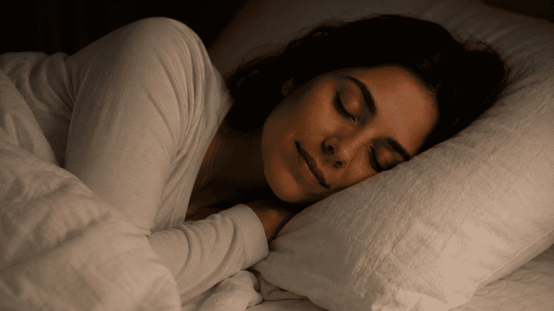 A person resting peacefully in a dark quiet bedroom, representing the feeling of waking up genuinely rested after deep restorative sleep