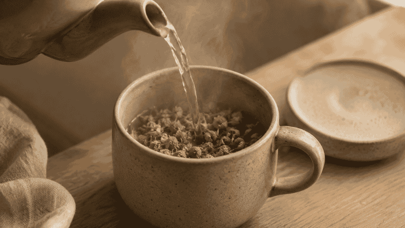 Hot water being poured from a kettle into a ceramic cup with a lid covering it to steep herbal tea, representing the correct brewing protocol for maximum sleep benefit