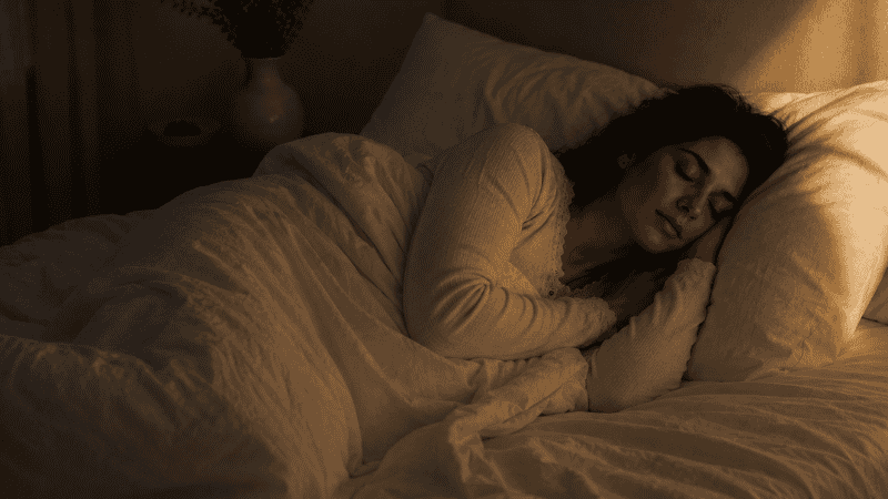 A new mother sleeping peacefully and deeply in a quiet dark bedroom with white linen, representing restful sleep recovery after postpartum insomnia