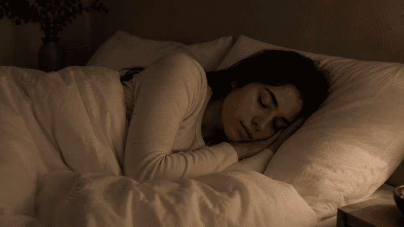 A person sleeping deeply and peacefully through the night in a dark calm bedroom with white linen, representing what adequate restorative sleep looks and feels like