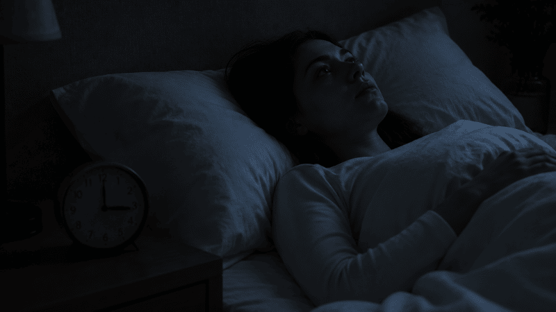A person lying awake in a dark bedroom staring at the ceiling with a clock showing 3am on the nightstand, representing the recurring pattern of waking up at 3am every night