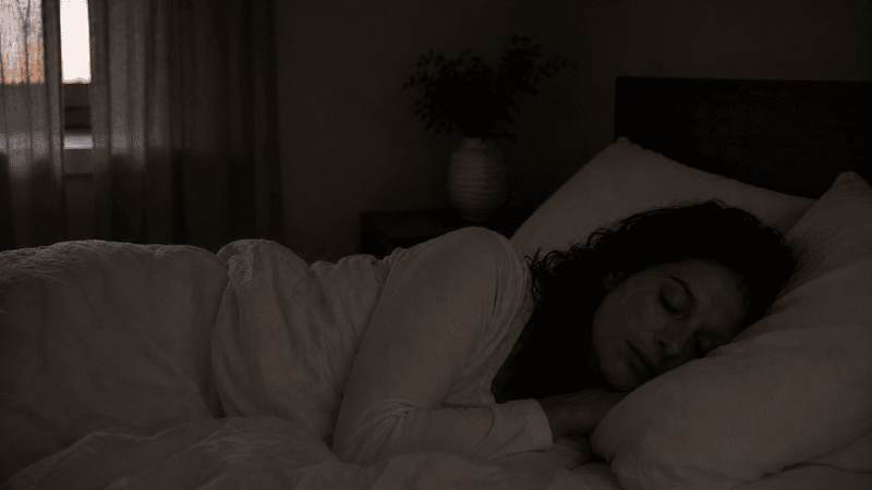A person sleeping deeply and undisturbed through the night in a dark calm bedroom, representing consolidated restorative sleep after resolving middle-of-the-night waking
