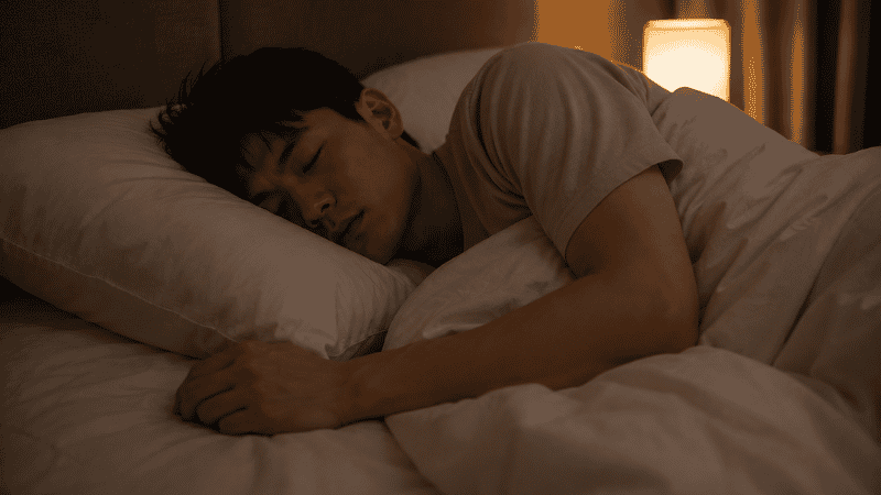 A person sleeping peacefully on their side in a dark calm bedroom with white linen bedding, representing the quiet rest that follows when nighttime anxiety has been successfully calmed