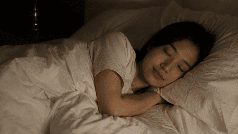 A person sleeping peacefully and deeply in a dark calm bedroom, representing the restoration of restful sleep after breaking the sleep-anxiety cycle