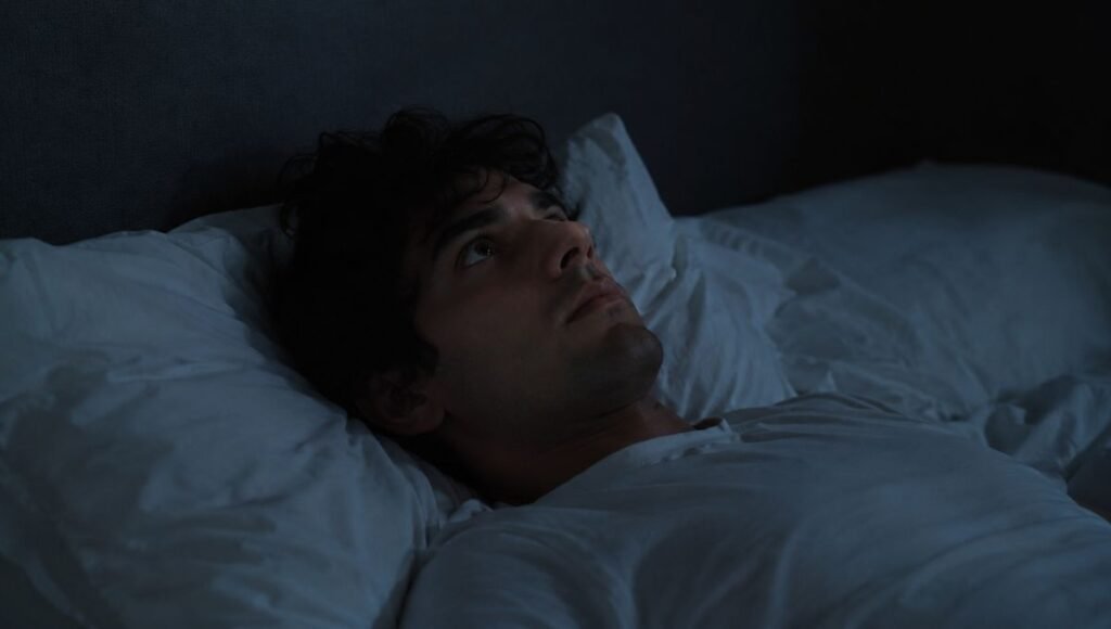A person lying awake in a dark bedroom at night with eyes open and a distant expression, representing the experience of overthinking at night when the brain won't stop